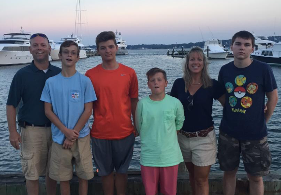 Parents and four boys standing in front of a marina with boats