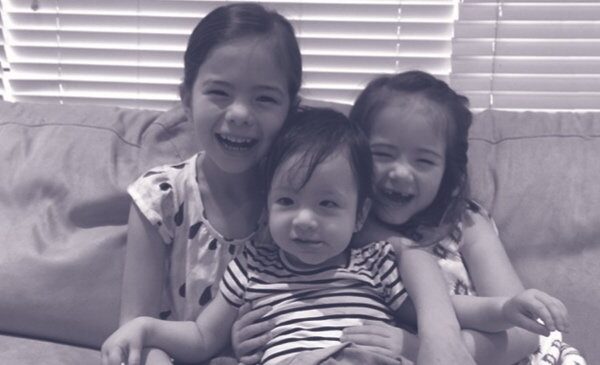 A black and white photo of three smiling young girls sitting on a couch. The youngest is visually impaired