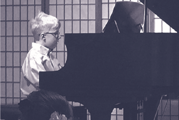 A black and white photo of a young boy with glasses playing a grand piano