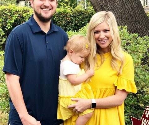 Young parents and their visually impaired baby daughter standing outside in front of bushes and a tree