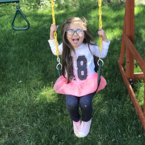 Young girl with glasses sitting on a swing and sticking her tongue out