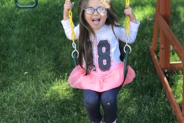 Young girl with glasses sitting on a swing and sticking her tongue out