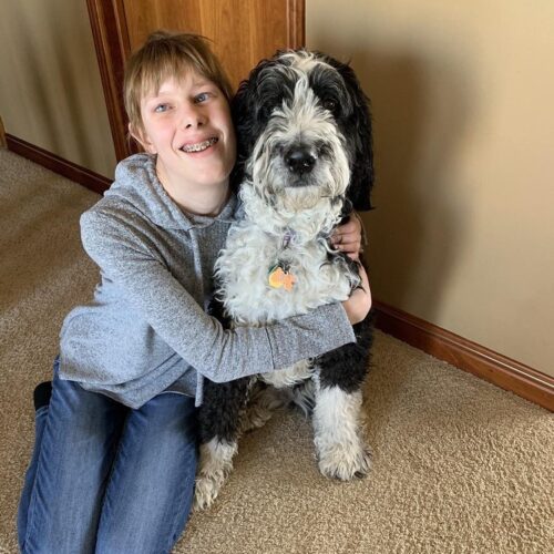 Visually impaired teenage girl sitting on the floor and hugging a black and white dog