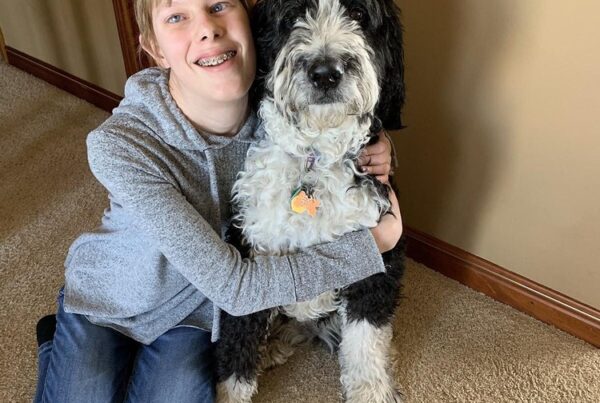 Visually impaired teenage girl sitting on the floor and hugging a black and white dog