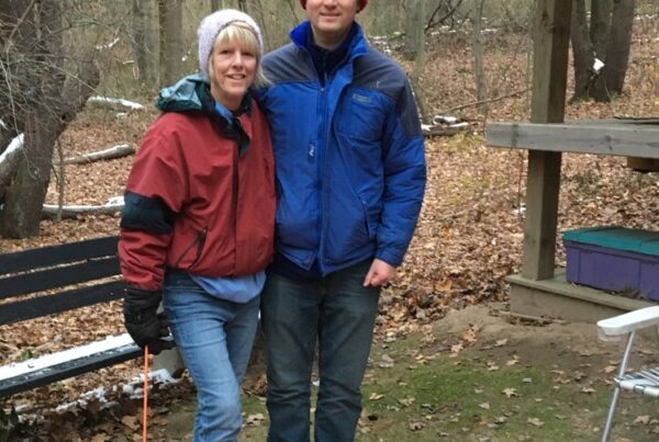 Mother and visualy impaired teenage son standing in front of a campfire at a campsite