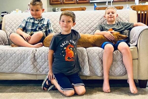 Three smiling brothers, one visually impaired, and a dog on a couch