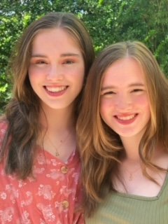 Two smiling sisters standing in front of a bush