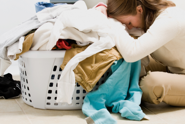 A woman sitting on the floor with her head in a laundry basket full of clothing