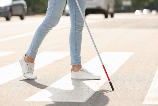 Women walking in a crosswalk with a white cane
