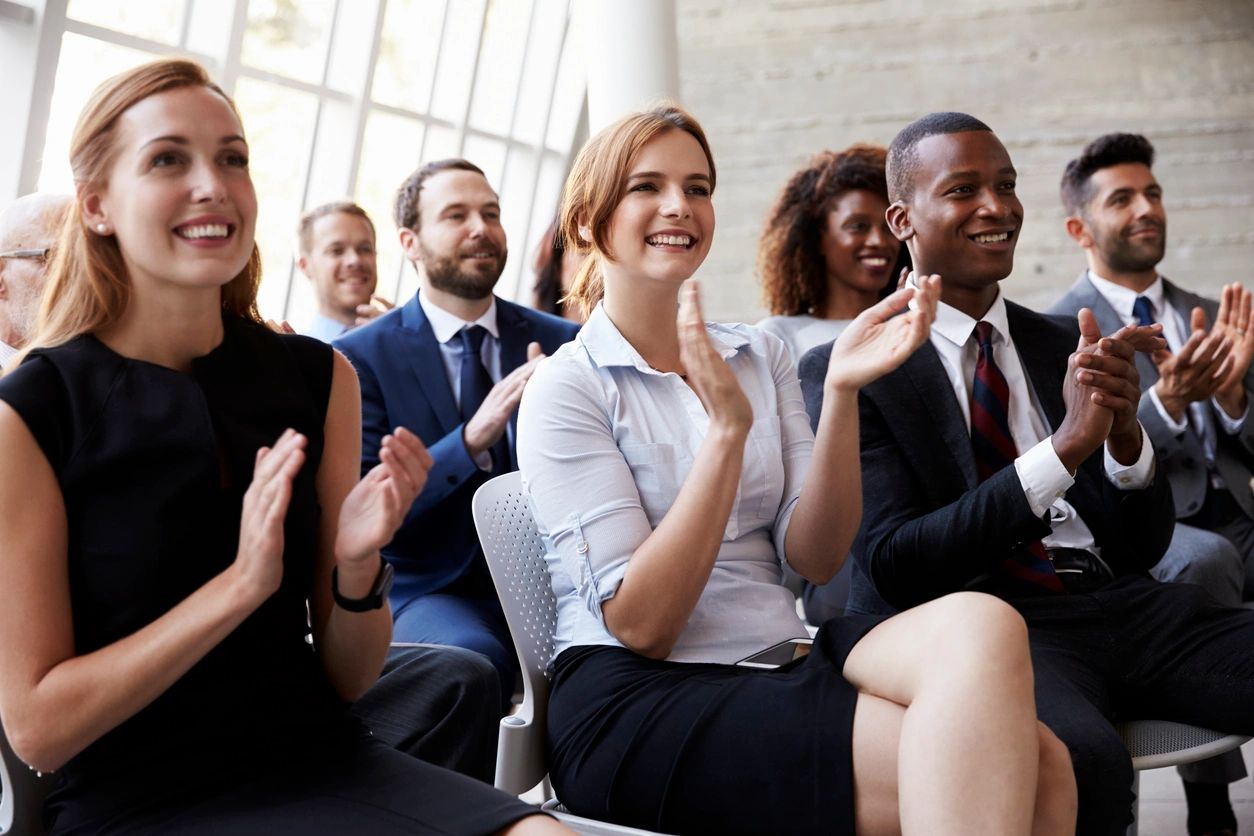 Professionals sitting in a seminar smiling and clapping