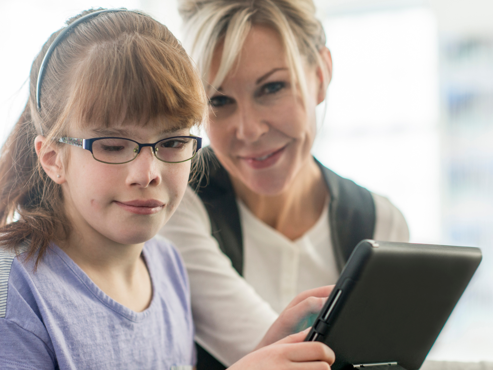 A smiling female teacher and young female visually impaired student with glasses holding a black technical device