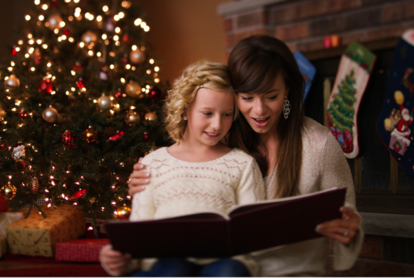 Mother reading a book to her daughter in front of a Christmas tree and Christmas stockings