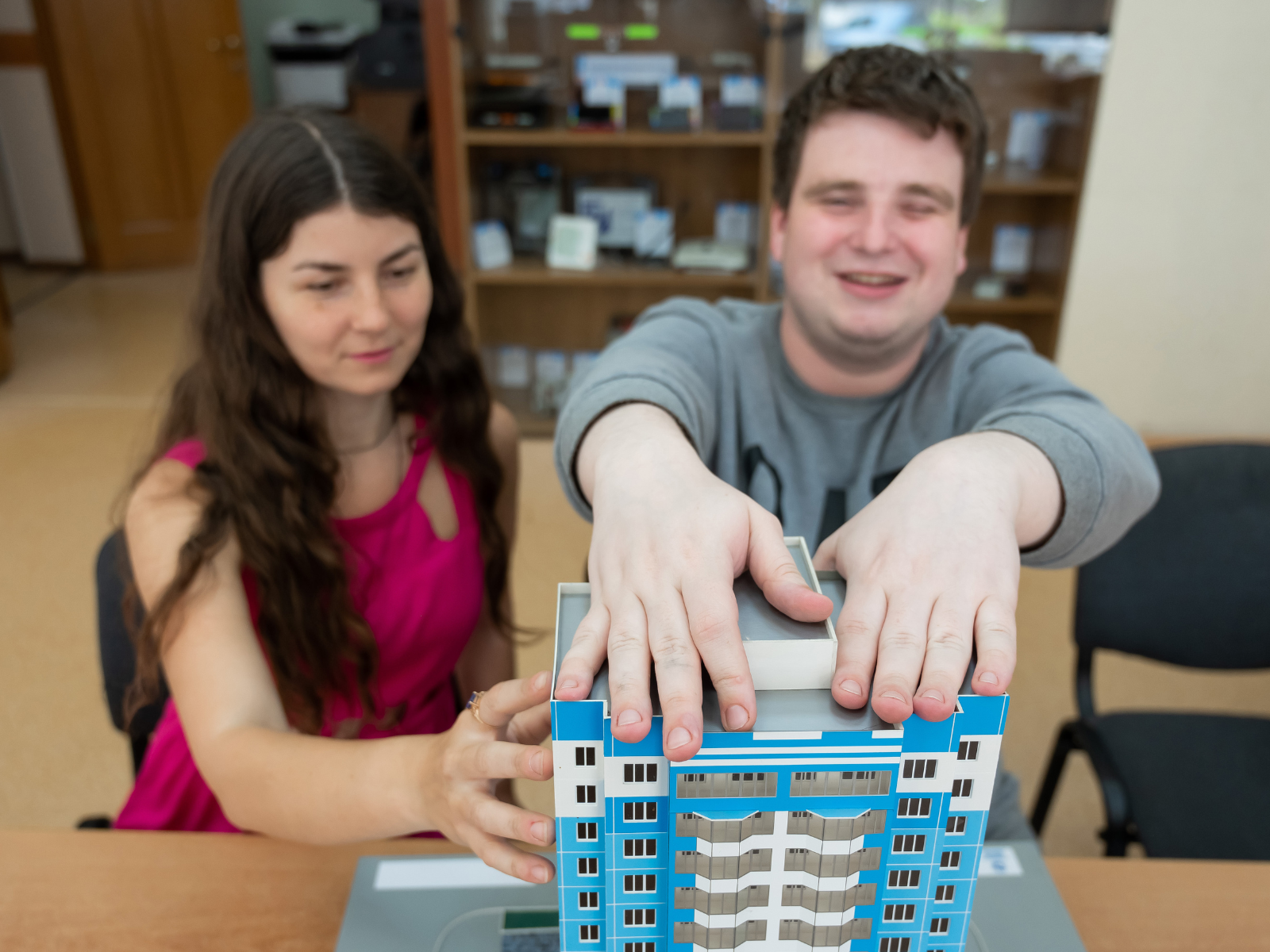 A female teacher and visually impaired male student who is touching a model building located on the desk in front of him