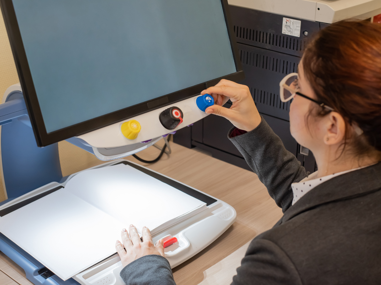 Woman with glasses adjusting a know on a technical device designed for visually impaired