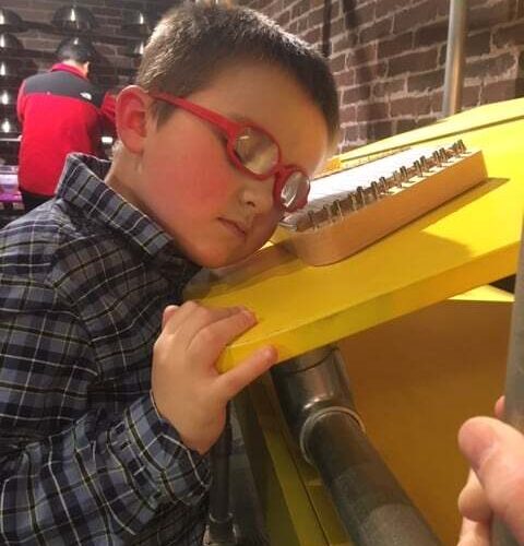 A young boy with red glasses listening to a wooden xylophone