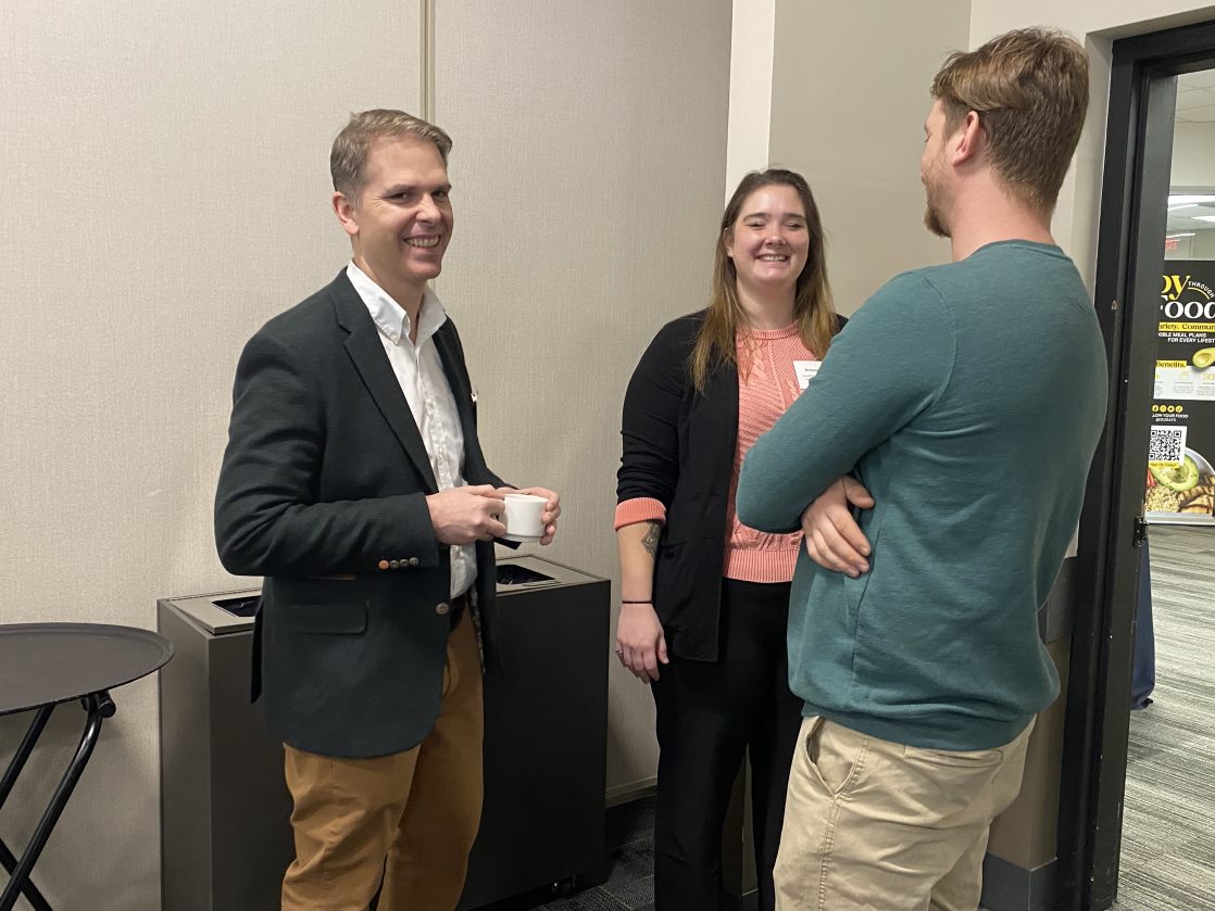 A group of three smiling professionally dressed adults talking in an office