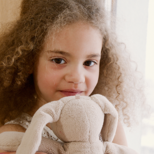 Smiling young girl with brown curly hair holding a stuffed bunny toy