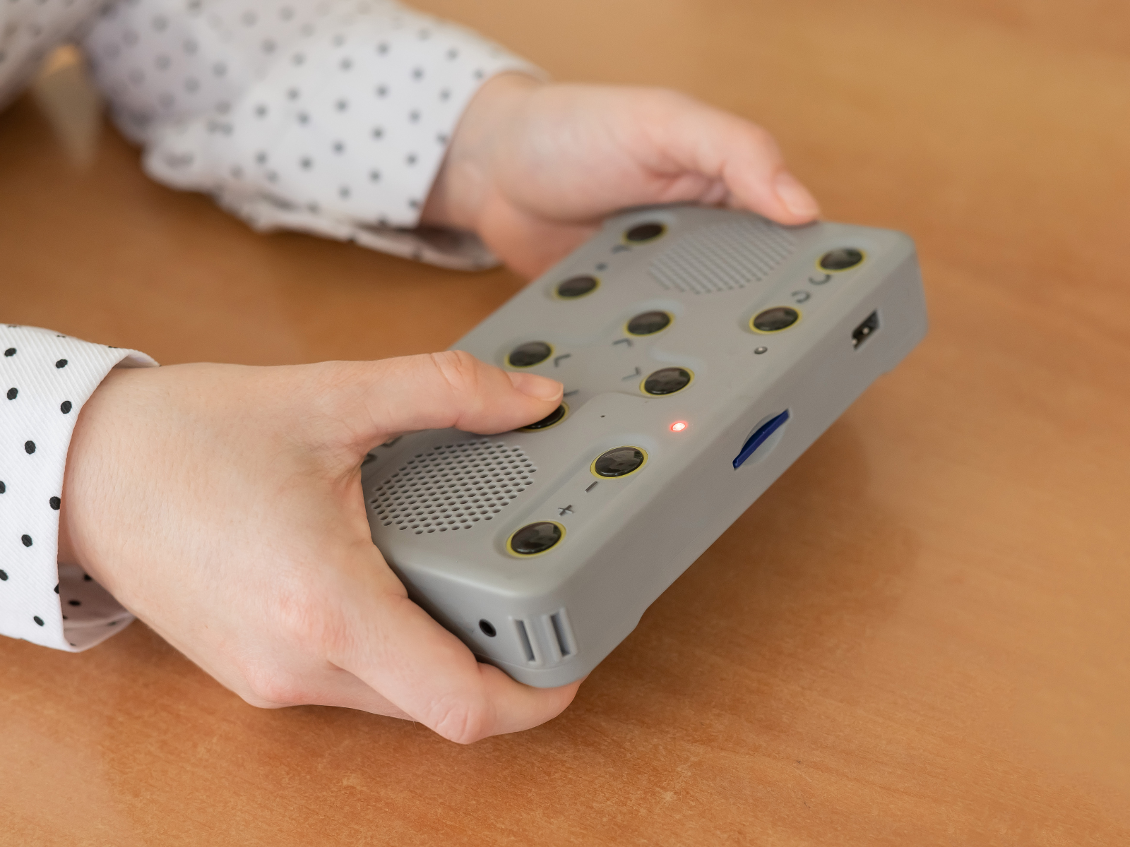 Hands holding rectangle grey electronic device designed for visually impaired
