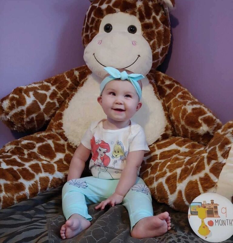 Smiling visually impaired 9 month old girl sitting in front a giant giraffe stuffed animal