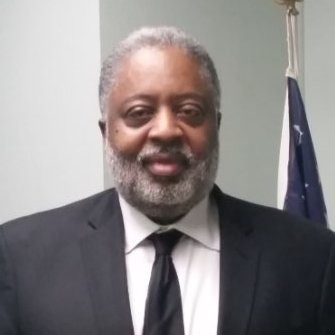 Man in suit, Bob McPherson, smiles for the camera, he has dark skin and a beard.